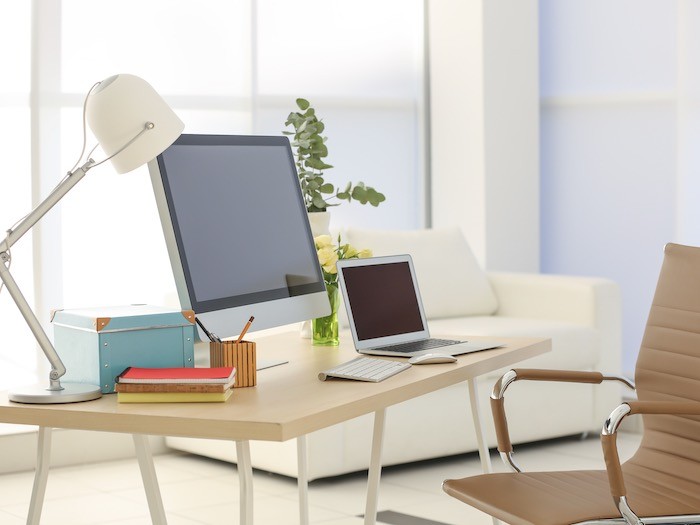 A desk facing natural light with a computer and desk lamp.